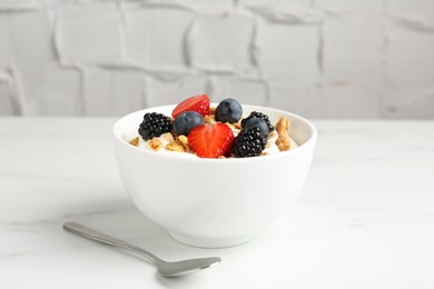Photo of Tasty yogurt with granola and berries in bowl on white marble table, closeup