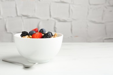 Photo of Tasty yogurt with granola and berries in bowl on white marble table, closeup. Space for text