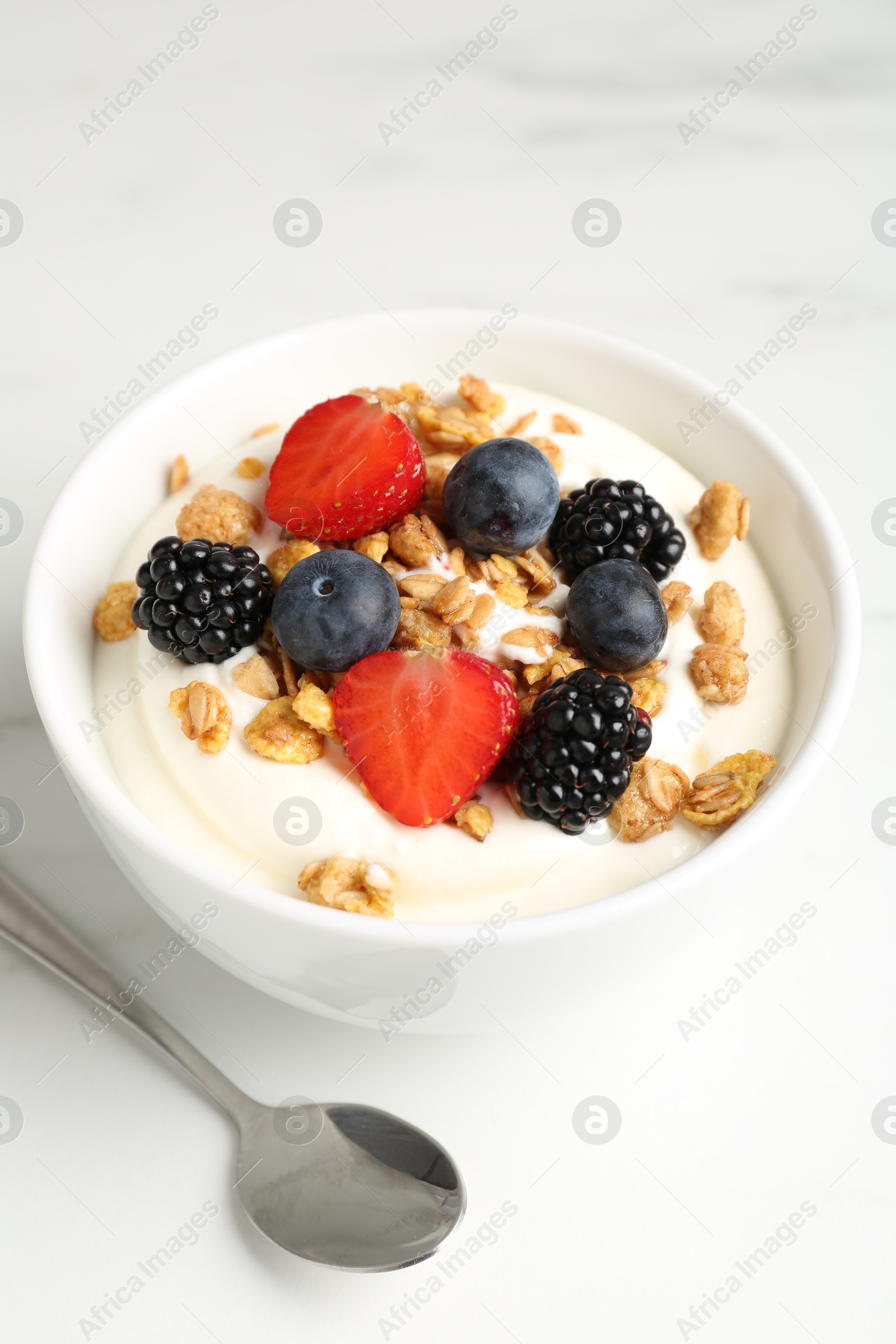 Photo of Tasty yogurt with granola and berries in bowl on white marble table, closeup