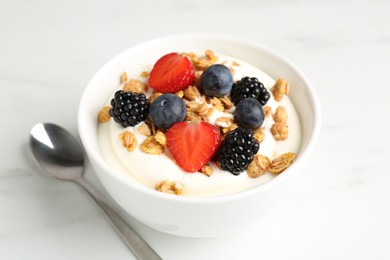 Photo of Tasty yogurt with granola and berries in bowl on white marble table, closeup