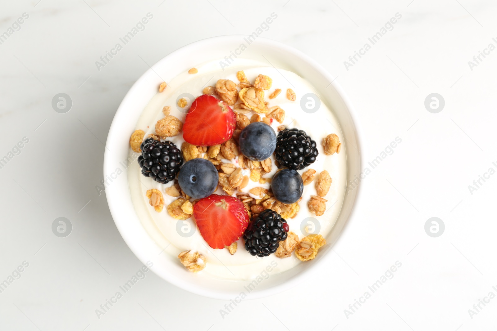 Tasty yogurt with granola and berries in bowl on white marble table, top view Photo of Tasty yogurt with granola and berries in bowl on white marble table, top view