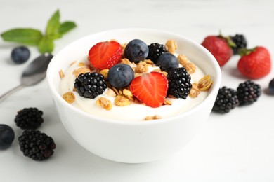 Photo of Tasty yogurt with granola and berries in bowl on white table, closeup