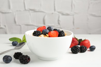 Photo of Tasty yogurt with granola and berries in bowl on white table, closeup