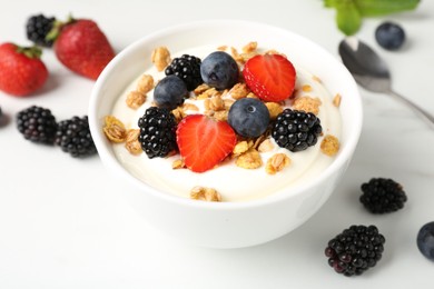 Photo of Tasty yogurt with granola and berries in bowl on white table, closeup