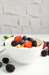 Photo of Tasty yogurt with granola and berries in bowl on white table, closeup. Space for text