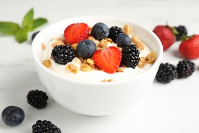 Photo of Tasty yogurt with granola and berries in bowl on white table, closeup