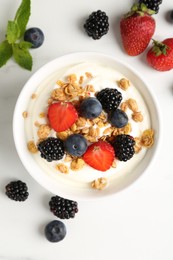 Photo of Tasty yogurt with granola and berries in bowl on white table, flat lay
