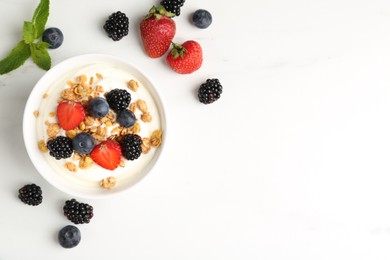 Photo of Tasty yogurt with granola and berries in bowl on white marble table, flat lay. Space for text
