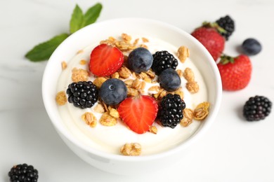 Photo of Tasty yogurt with granola and berries in bowl on white marble table, closeup