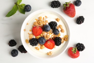 Photo of Tasty yogurt with granola and berries in bowl on white marble table, flat lay