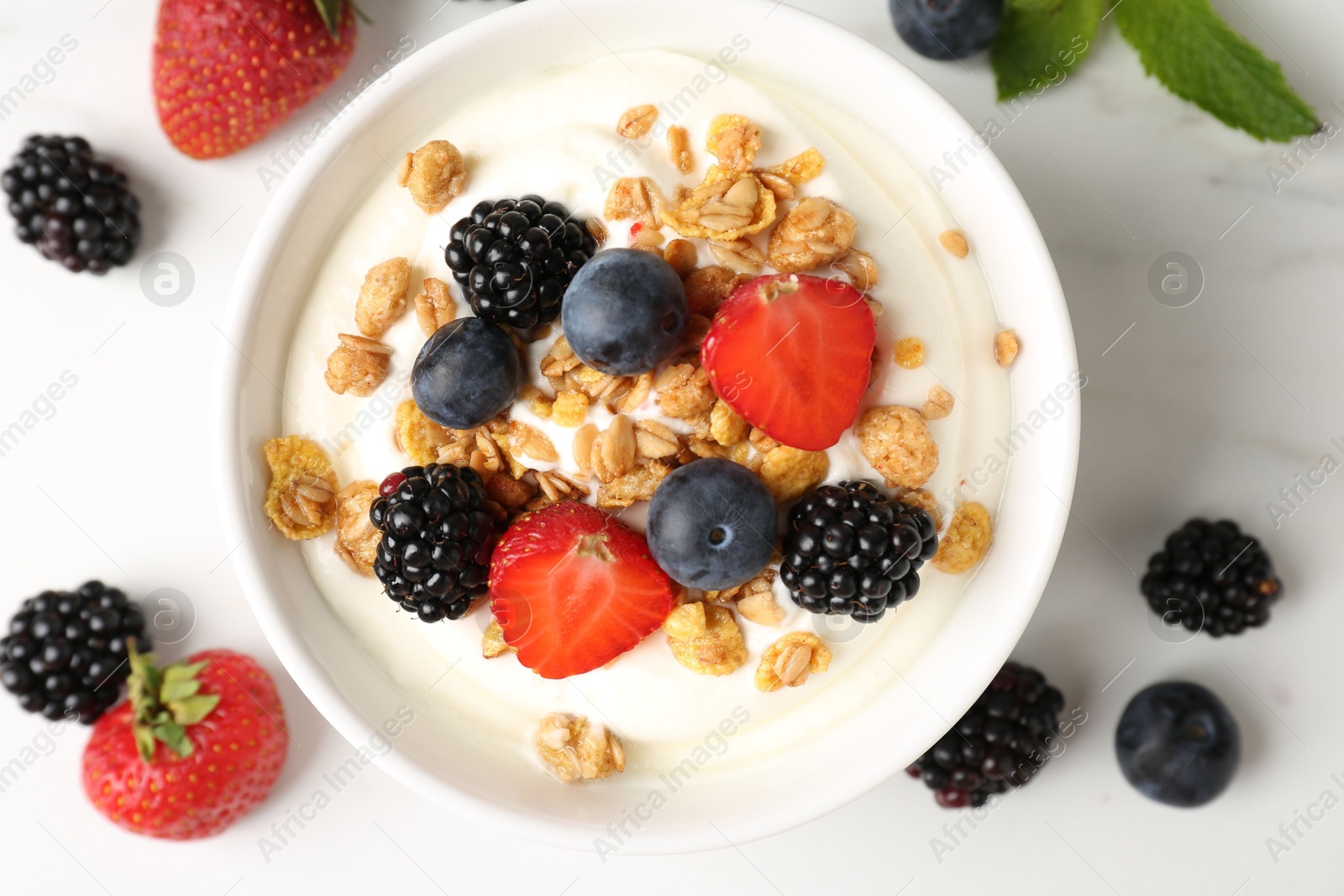 Tasty yogurt with granola and berries in bowl on white marble table, flat lay Photo of Tasty yogurt with granola and berries in bowl on white marble table, flat lay