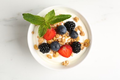 Photo of Tasty yogurt with granola and berries in bowl on white marble table, top view