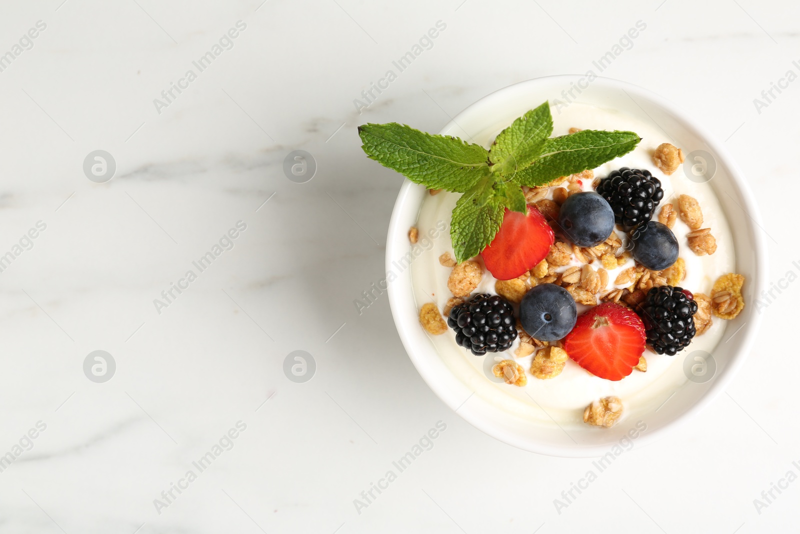 Tasty yogurt with granola and berries in bowl on white marble table, top view. Space for text Photo of Tasty yogurt with granola and berries in bowl on white marble table, top view. Space for text