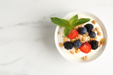 Photo of Tasty yogurt with granola and berries in bowl on white marble table, top view. Space for text