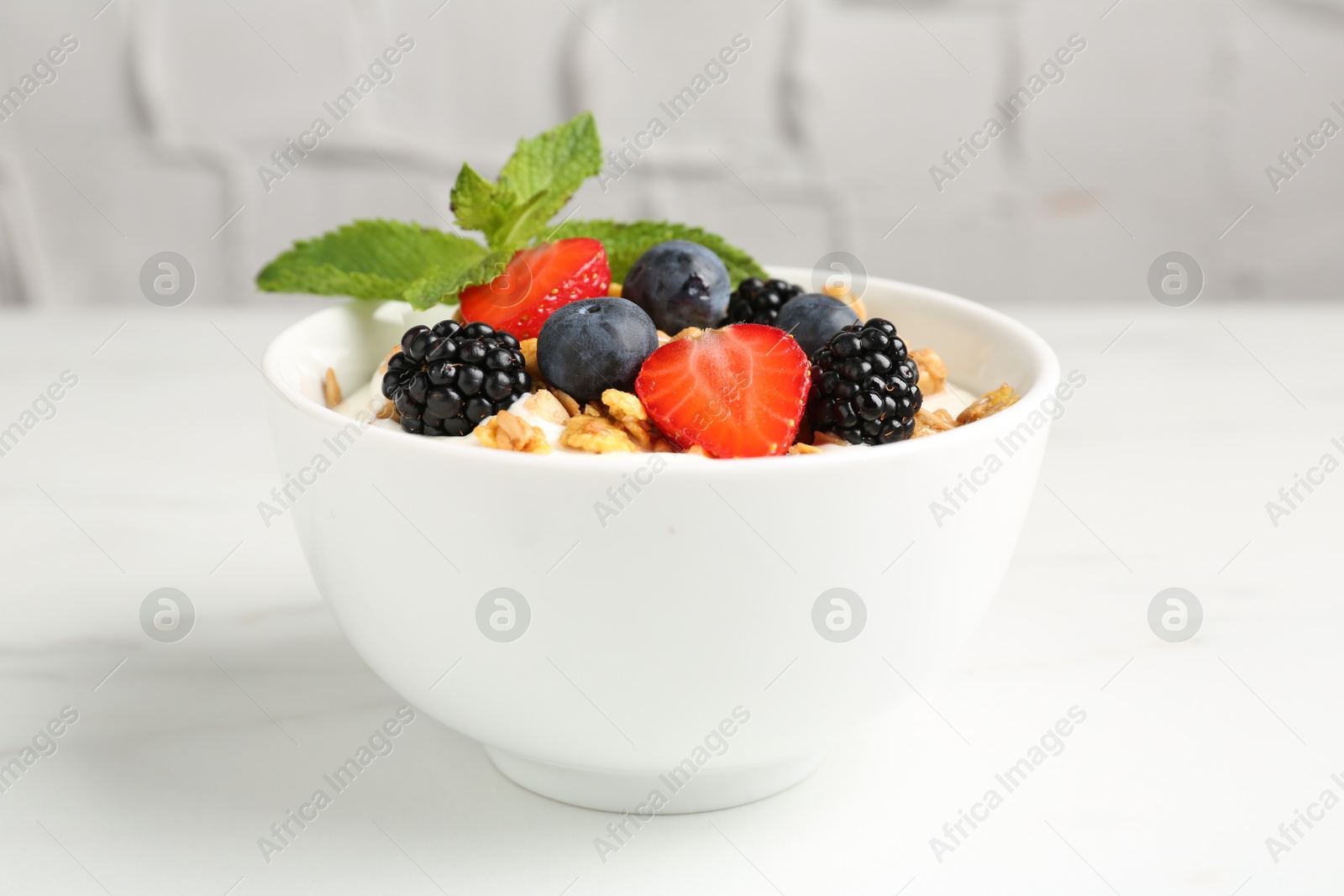 Photo of Tasty yogurt with granola and berries in bowl on white marble table, closeup