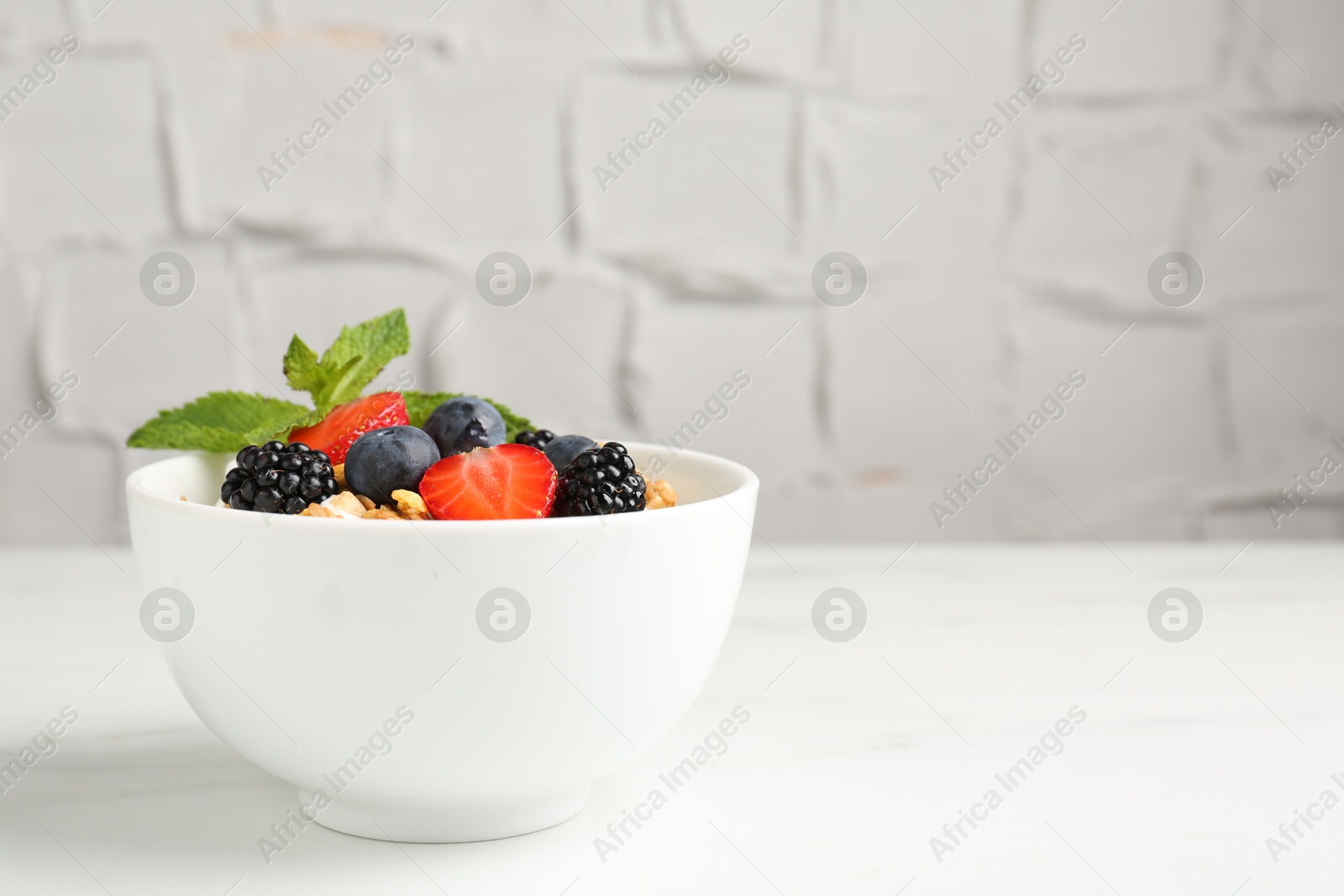 Photo of Tasty yogurt with granola and berries in bowl on white marble table, closeup. Space for text