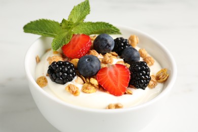 Photo of Tasty yogurt with granola and berries in bowl on white marble table, closeup
