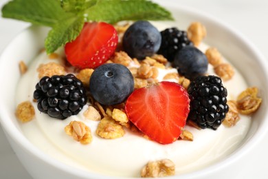 Photo of Tasty yogurt with granola and berries in bowl on white table, closeup
