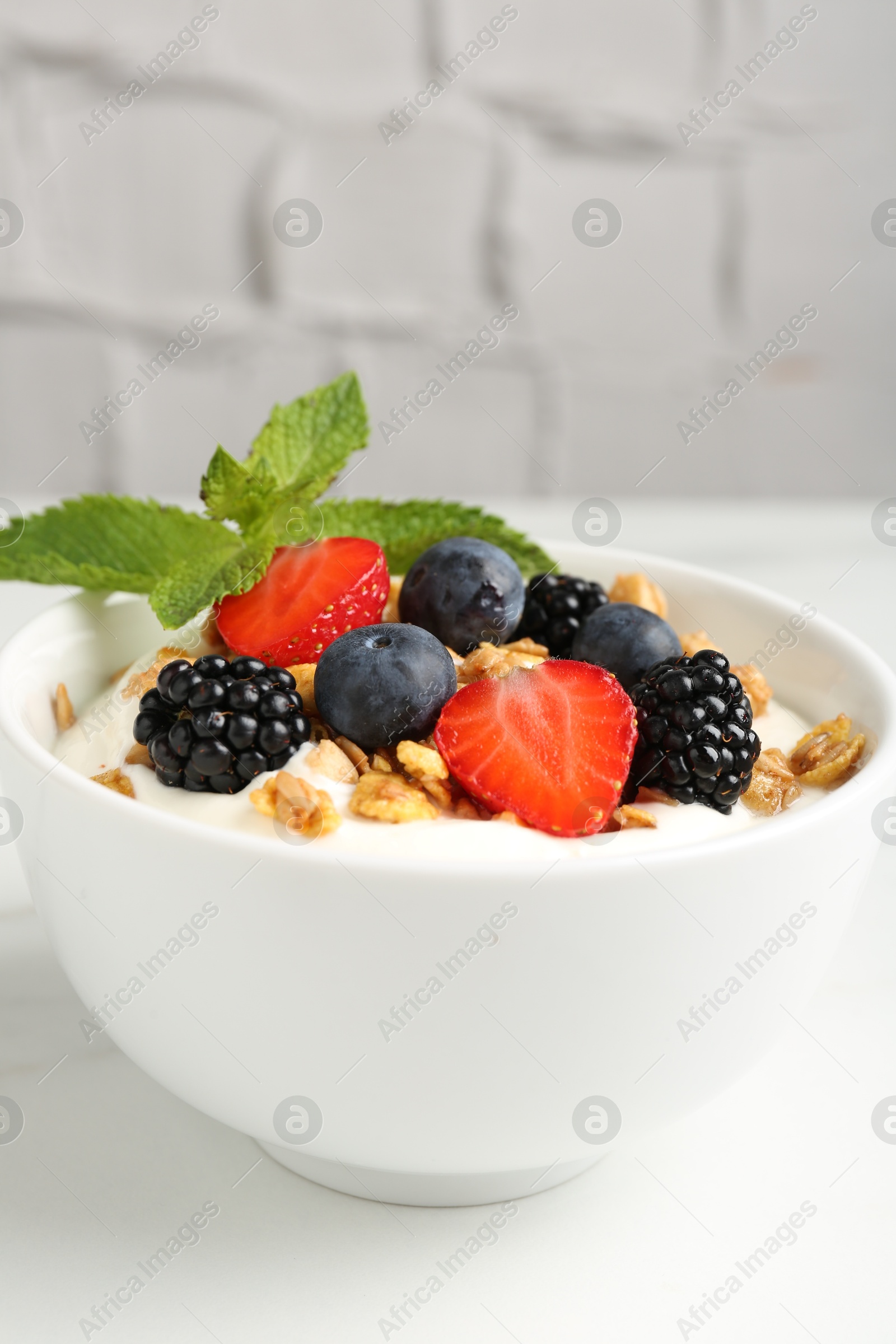 Photo of Tasty yogurt with granola and berries in bowl on white table, closeup