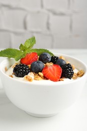 Photo of Tasty yogurt with granola and berries in bowl on white table, closeup