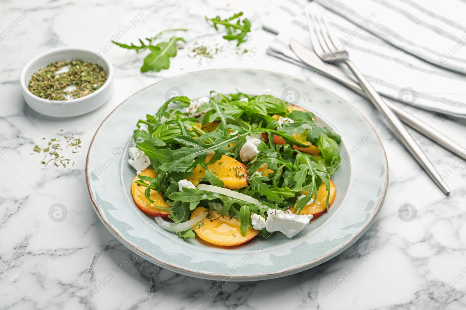 Tasty salad with arugula, cheese, peach, basil and spices on white marble table, closeup Photo of Tasty salad with arugula, cheese, peach, basil and spices on white marble table, closeup