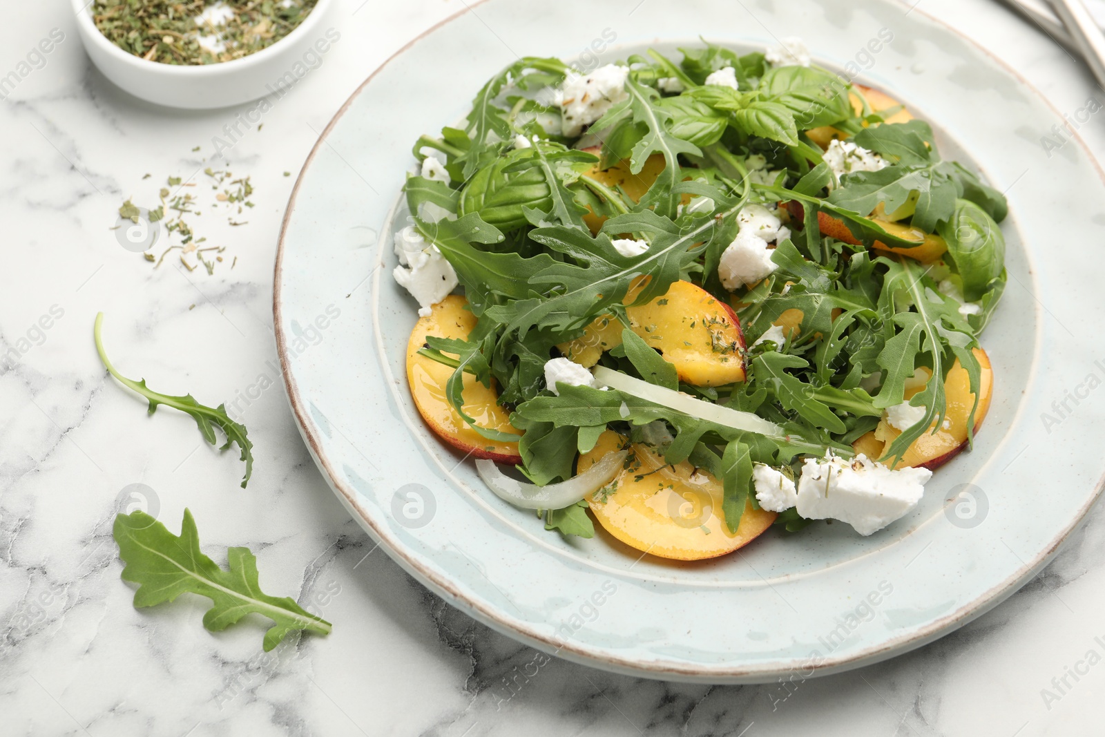 Tasty salad with arugula, cheese, peach, basil and spices on white marble table, above view Photo of Tasty salad with arugula, cheese, peach, basil and spices on white marble table, above view