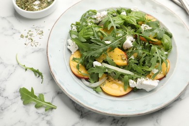 Photo of Tasty salad with arugula, cheese, peach, basil and spices on white marble table, above view