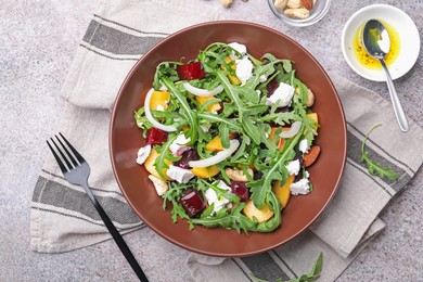 Photo of Tasty salad with arugula, cheese, peach, beetroot and nuts on grey table, flat lay