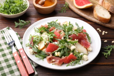 Photo of Tasty salad with arugula, prosciutto, cheese, pear, grapefruit and nuts on wooden table, closeup