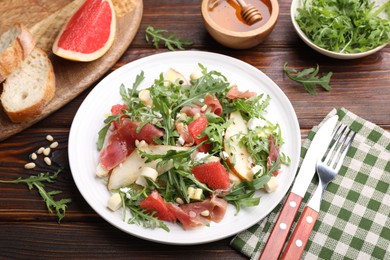 Photo of Tasty salad with arugula, prosciutto, cheese, pear, grapefruit and nuts on wooden table, above view