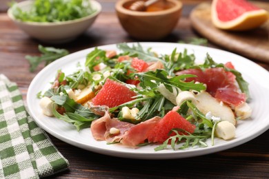 Photo of Tasty salad with arugula, prosciutto, cheese, pear, grapefruit and nuts on wooden table, closeup