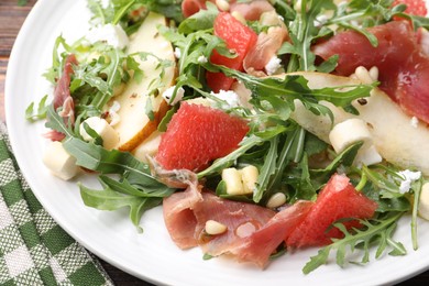Photo of Tasty salad with arugula, prosciutto, cheese, pear, grapefruit and nuts on table, closeup