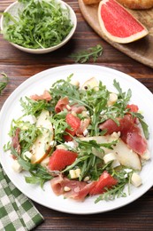 Photo of Tasty salad with arugula, prosciutto, cheese, pear, grapefruit and nuts on wooden table, above view