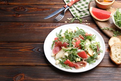 Photo of Tasty salad with arugula and prosciutto served on wooden table, closeup. Space for text