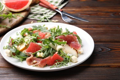 Photo of Tasty salad with arugula, prosciutto, cheese, pear, grapefruit and nuts on wooden table, closeup