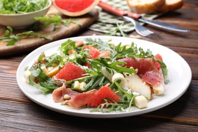 Photo of Tasty salad with arugula, prosciutto, cheese, pear, grapefruit and nuts on wooden table, closeup