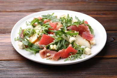 Photo of Tasty salad with arugula, prosciutto, cheese, pear, grapefruit and nuts on wooden table, closeup