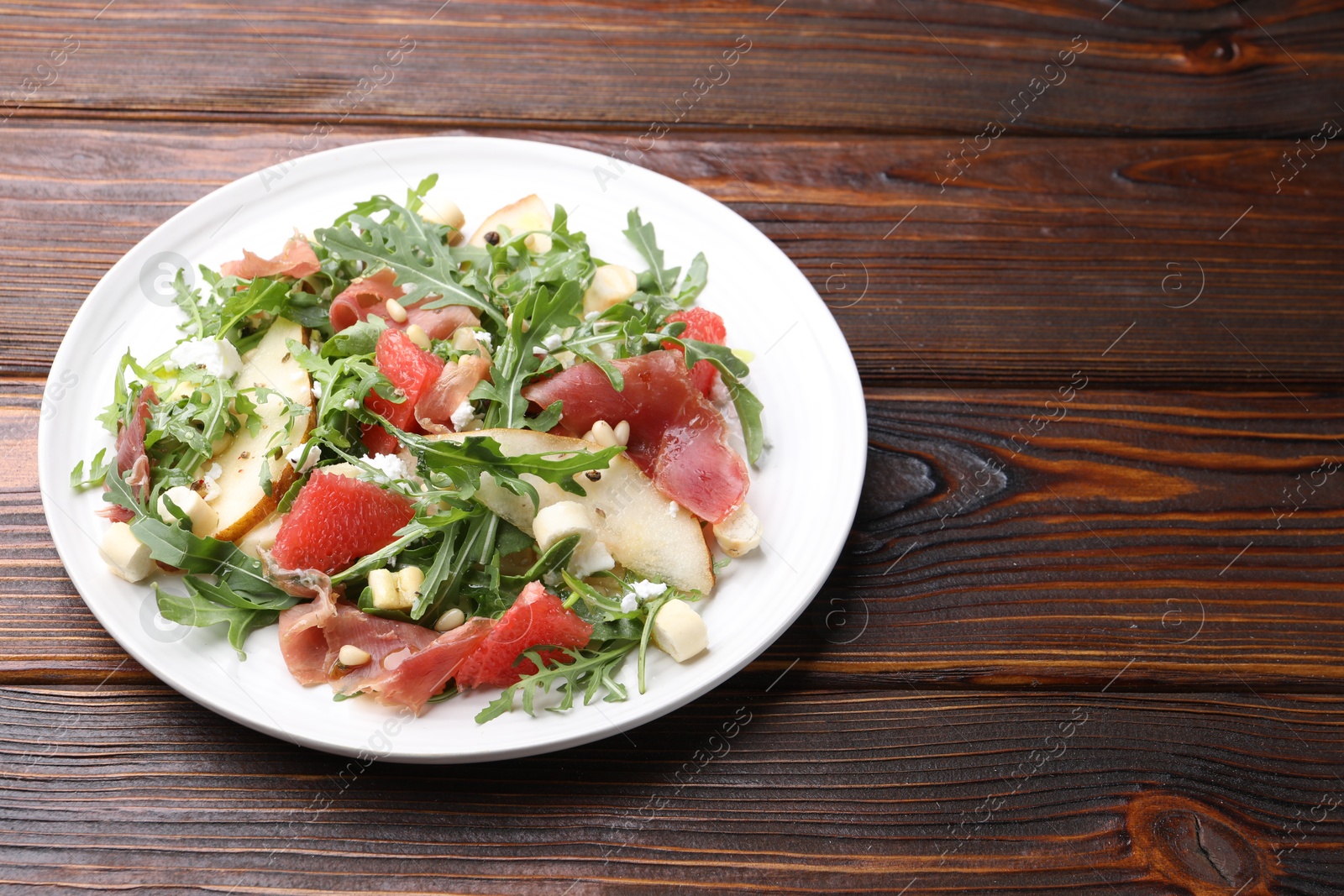 Tasty salad with arugula, prosciutto, cheese, pear, grapefruit and nuts on wooden table, closeup. Space for text Photo of Tasty salad with arugula, prosciutto, cheese, pear, grapefruit and nuts on wooden table, closeup. Space for text