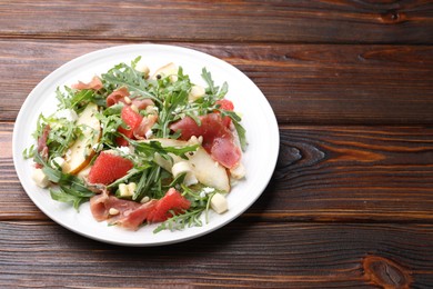 Photo of Tasty salad with arugula, prosciutto, cheese, pear, grapefruit and nuts on wooden table, closeup. Space for text