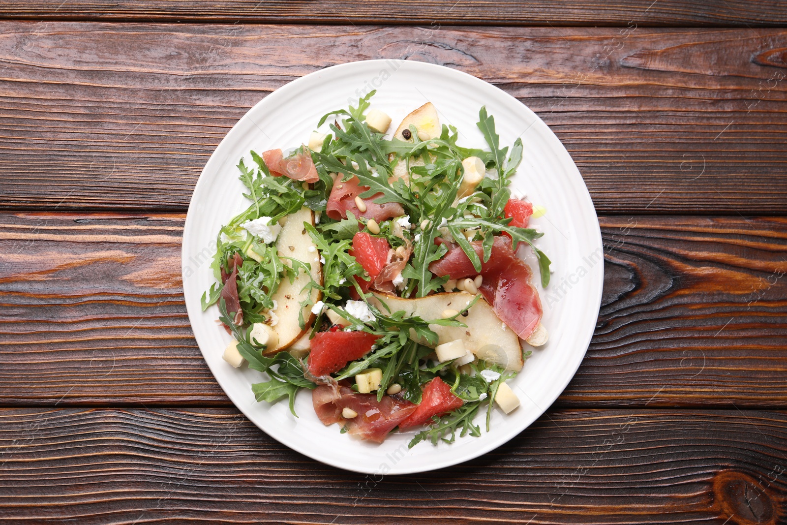 Tasty salad with arugula, prosciutto, cheese, pear, grapefruit and nuts on wooden table, top view Photo of Tasty salad with arugula, prosciutto, cheese, pear, grapefruit and nuts on wooden table, top view
