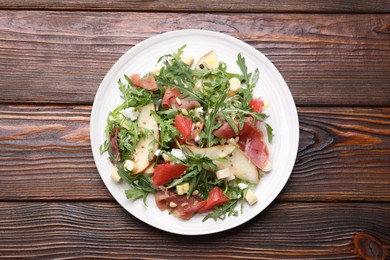 Photo of Tasty salad with arugula, prosciutto, cheese, pear, grapefruit and nuts on wooden table, top view