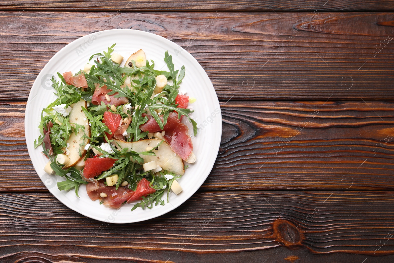 Tasty salad with arugula, prosciutto, cheese, pear, grapefruit and nuts on wooden table, top view. Space for text Photo of Tasty salad with arugula, prosciutto, cheese, pear, grapefruit and nuts on wooden table, top view. Space for text