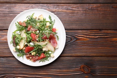 Photo of Tasty salad with arugula, prosciutto, cheese, pear, grapefruit and nuts on wooden table, top view. Space for text