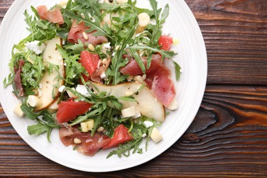 Photo of Tasty salad with arugula, prosciutto, cheese, pear, grapefruit and nuts on wooden table, top view