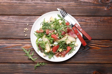 Photo of Tasty salad with arugula, prosciutto, cheese, pear, grapefruit and nuts on wooden table, top view