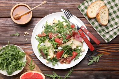 Photo of Tasty salad with arugula and prosciutto served on wooden table, flat lay