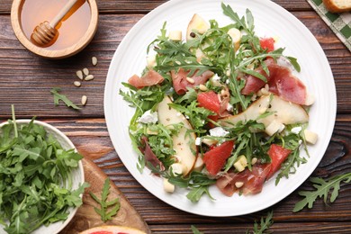 Photo of Tasty salad with arugula and prosciutto served on wooden table, flat lay