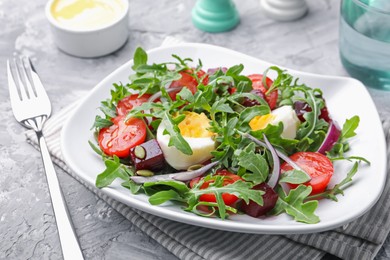 Photo of Tasty salad with arugula, vegetables and egg served on grey table, closeup