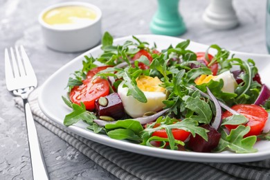 Photo of Tasty salad with arugula, vegetables and egg served on grey table, closeup