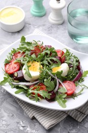 Photo of Tasty salad with arugula, vegetables and egg served on grey table, closeup